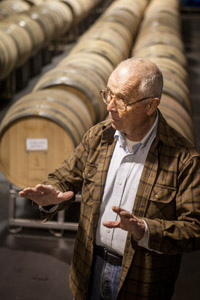 George Hendry, Owner and Winemaker, standing in front of rows of wine barrels in the cellar