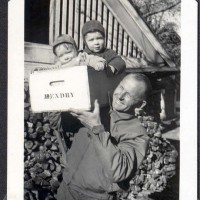 Vintage picture of a smiling man carrying two toddlers (George and Andy Hendry) in a wooden grape box.